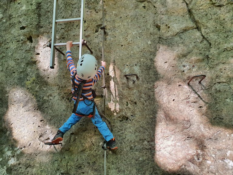 Ein kleines Kind hängt am Felsen und versucht eine Leiter hochzuklettern.