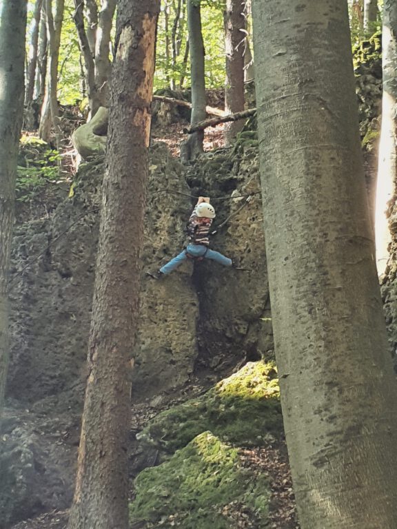 Ein Kind hängt mit Kletterausrüstung am Felsen.