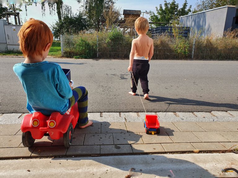 Zwei Kinder spielen auf der Straße mit Autos.